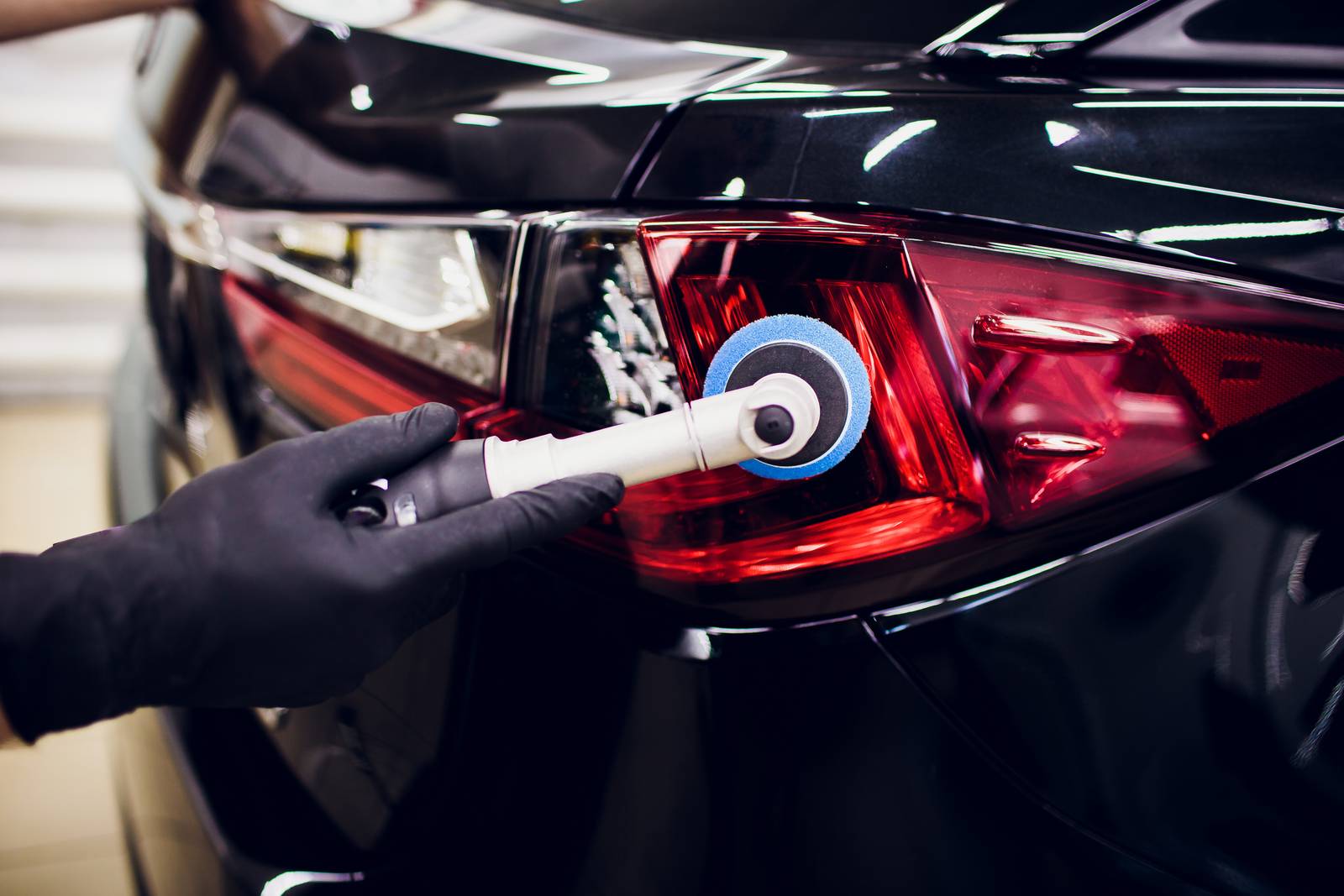 Car polish wax worker hands holding polisher and polish car detailing or valeting concept taillight red car